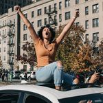 A Black woman raises her arms in victory will sitting through a sunroof of a car